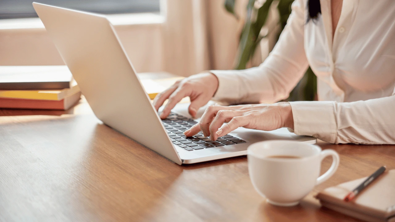 Close-up shot of hands actively typing on a laptop keyboard in a bright workspace environment.