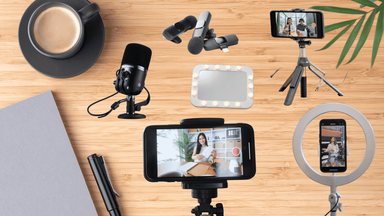 Flat lay of content creation gear on a wooden desk, including a coffee cup, microphone, tripod, ring light, and smartphones.