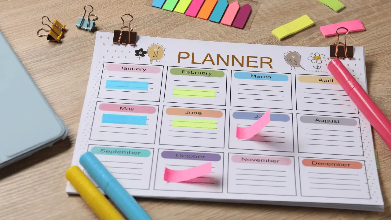 Flat lay workspace showcasing an annual planner layout with sticky notes, highlighters, and binder clips.